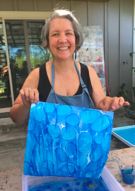 Jocelyn holds a piece of paper marbled with different shades of blue, smiling