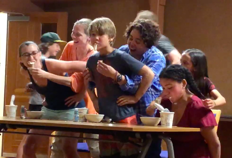 Three people stand behind three other people, feeding the people in front ice cream cones.