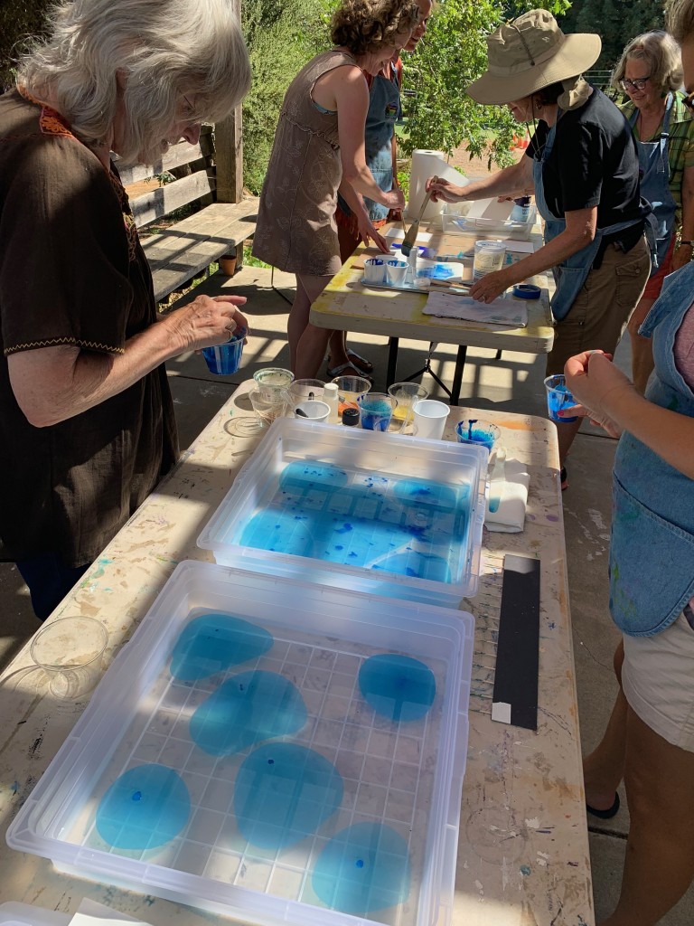 People are gathered around bins of water with blue dye, preparing to marble paper